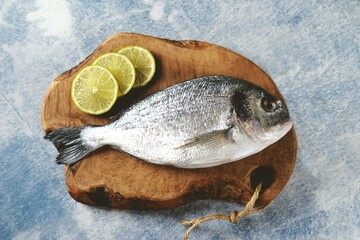 Fresh uncooked dorado with lime, salt and pepper on an olive board.