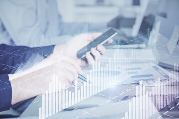 Double exposure of man's hands holding and using a digital device and forex graph drawing. Financial market concept.