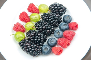 berries raspberries, blueberries, gooseberries and blackberries on a white plate. useful vitamin healthy food fruit. healthy vegetable breakfast
