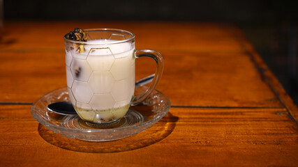 A glass of hot ginger milk on a wooden table. A special drink from Indonesia, pure milk mixed with grilled ginger