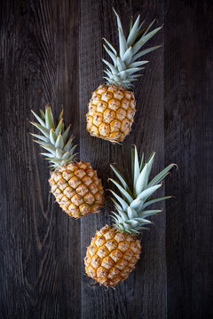 Three Pineapple on the dark wood backdrop, top-down photography, simple and classy