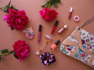 Trendy girl content. Female fashion and cosmetics accessories. Woman bag, lipsticks, serum, facial roller, nail polish and scrunchy on dark pink background with pink peony flowers.  © SveM