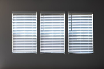 Three windows with closed modern white wood faux window blinds as background.