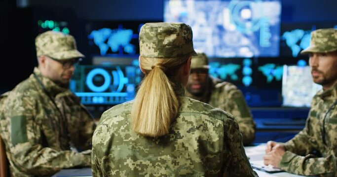 Rear of female general giving orders to mixed-races males militarian council at table. Deciding war or defense tactics in monitoring room. Back view Woman and multiethnic officers discussing terrorism
