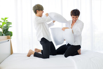 Homosexual men or gay couples with pillows battle on the bed.