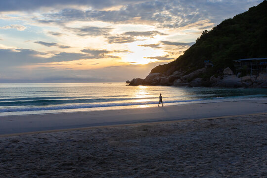 Young woman is walking alone on the beach during sunrise. Phangan island, Thailand.