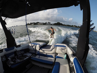 Surfer transfer wave surfing behind boat, interior of boat and seats in the foreground