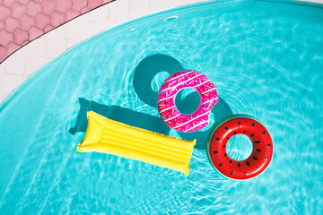 Fototapeta na wymiar Inflatable rings and mattress floating in swimming pool, top view. Summer vacation