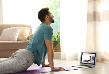 Distance yoga course during coronavirus pandemic. Man having online practice with instructor via laptop at home