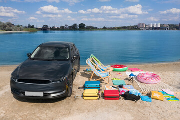 Car and beach accessories on sand near river. Summer trip