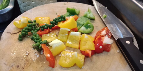 Condiments, vegetables, red and green chilies, fresh green peppers, tomatoes on a wooden cutting board.