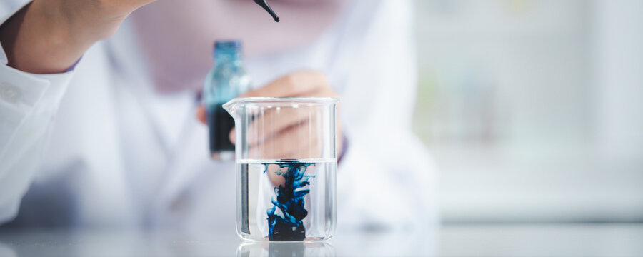 Woman scientist doing the experiment in laboratory, scientist dropping blue chemical into experiment glass bottle close up.