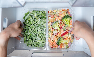 Hands are taking a container of frozen vegetables from the freezer of the fridge. Concept of...