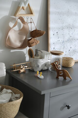 Wooden toys and different accessories on grey chest of drawers in child room