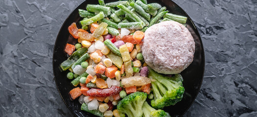 Plate of frozen vegetables and a meat cutlet on a gray table. Concept of saving time on cooking...