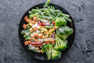Plate of frozen vegetables on a gray table. Concept of saving time on cooking dinner and convenient...