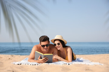 Fototapeta premium Happy couple reading book together on sunny beach