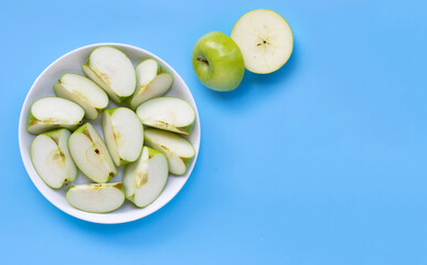 Fresh green apple slices on white plate on blue background.