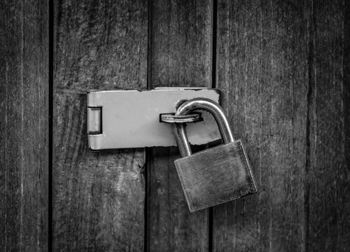Locked padlock with chain at gray wooden door. black and white.