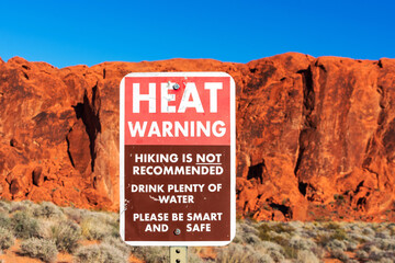 Extreme Heat warning sign informs tourists of the dangers of heat exhaustion from hiking in the desert climate. Blurred scenic red sandstone formations and desert scrub landscape background. Blue sky