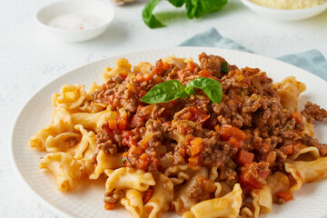 Pasta Bolognese campanelle with mincemeat and tomato sauce, parmesan cheese, basil. Italian dinner, white table. , side view, close up