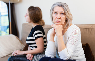 Frustrated mother and adult daughter sitting on sofa after quarrel