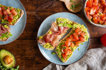 Avocado spread with chopped tomatoes and herbs. Parma prosciutto ham. Healthy breakfast seen from above.