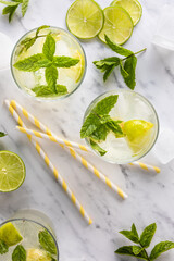 Mojito cocktail or mocktail, traditional fresh drink with lime and mint. With paper straws on the table. Top view, from above. On a white marble table.