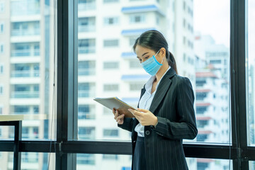 Fototapeta na wymiar Beautiful young Asian woman wearing protective mask to Protect Against Covid-19 working in office in modern office.