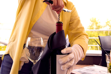 The waiter in the restaurant on the terrace opens a bottle of wine with a corkscrew