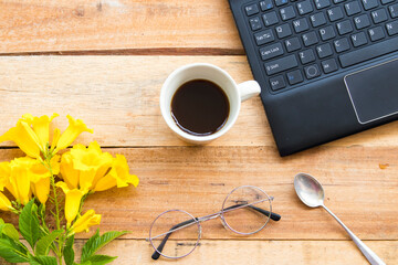 office supplies computer notebook for business work with hot coffee ,yellow flowers arrangement at office on background wooden 