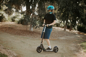 Young boy during the corona virus COVID-19 pandemic wearing a fabric mask and riding scooter