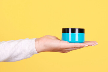 Hand with blue cream jar. Isolated on yellow background.