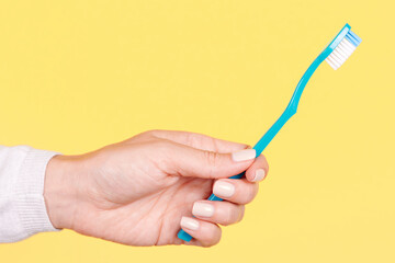 Hand with blue toothbrush, dental care. Isolated on yellow background.