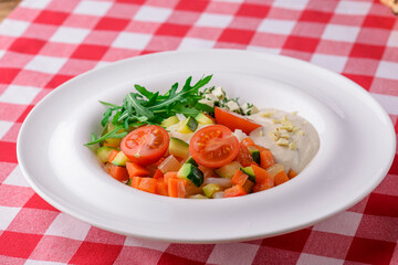 Fresh salad with radishes, lettuce, tomatoes and cucumbers sauce and fresh greenery served in a white plate.