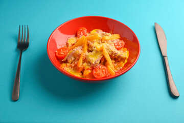 Melting cheddar cheese over the top of french fries covered in spicy sauce with meat and tomatoes. Blue background.