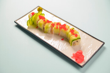 Green dragon sushi roll with eel, avocado, cucumber, wasabi sauce and ginger served on a white rectangular plate.