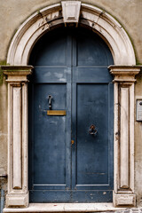 Wooden blue doors with a hole for mail, knocker and ring handle in an oval arch with door knocker.