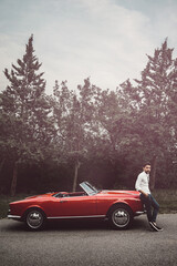 Young man standing near a Red Classic Car in the countryside