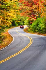 A red car driving through winding road with beautiful autumn foliage trees in New England - 369872174