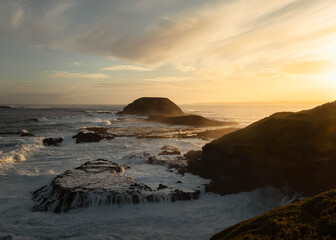 Rough elements going at each other at sunset in Australia, sea crushing into the rocks forming the coastline with an island in the background