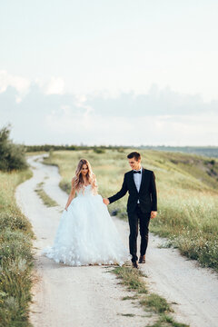 Bride and groom walking on the road. Full length body portrait of young bride and groom enjoying romantic moments outside at sunset in beautiful summer day. Wedding couple. 
