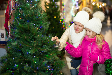 Pleasant woman with daughter buying Christmas tree in market. High quality photo