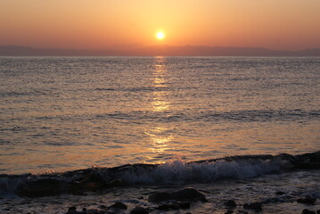 Beautiful dawn over the sea. The sun rises from behind the mountains. Sunny path on the water. Light wave and swell on the surface of the water