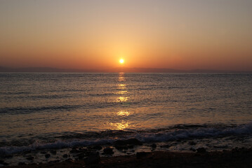 Obraz premium Beautiful dawn over the sea. The sun rises from behind the mountains. Sunny path on the water. Light wave and swell on the surface of the water