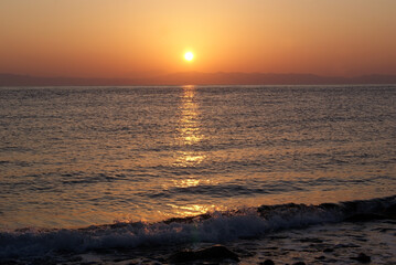 Obraz premium Beautiful dawn over the sea. The sun rises from behind the mountains. Sunny path on the water. Light wave and swell on the surface of the water