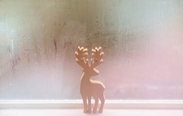 Raindrops on window glass and deer sculpture wood background.