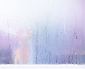 Raindrops on window glass and deer sculpture wood background.