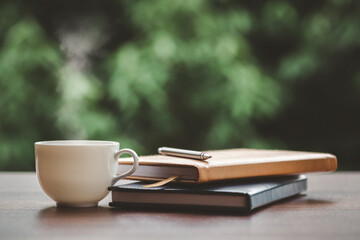 Hot coffee, smoke, with books and pens for note taking with beautiful nature background.