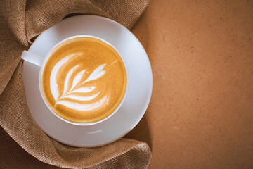 Latte art on cappuccino coffee cup with sackcloth on craft board.